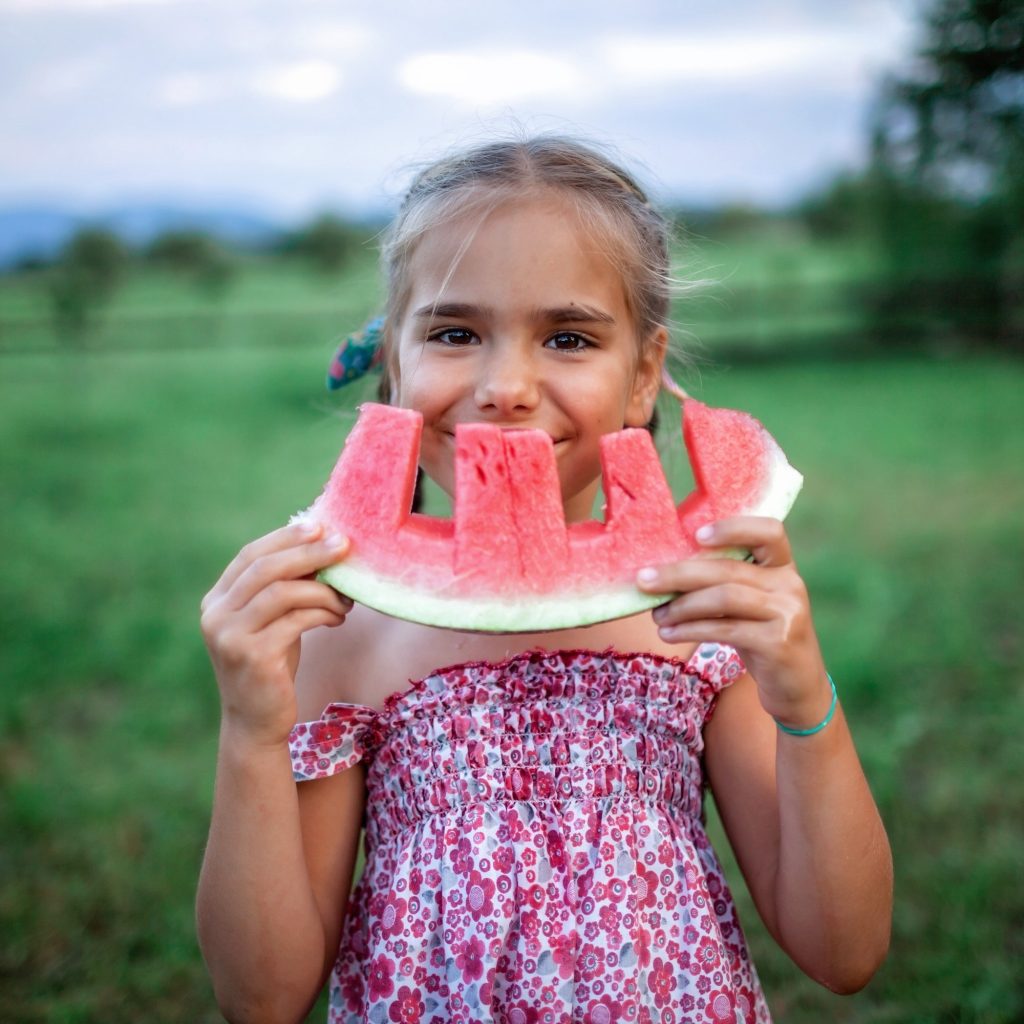 Healthy summer food. Cute kid biting a slice of watermelon in the backyard of farmhouse